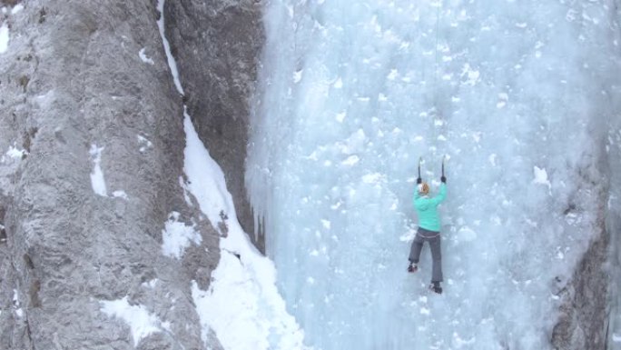 无人机，复制空间: 无畏的女人爬上华丽的冰冻瀑布。
