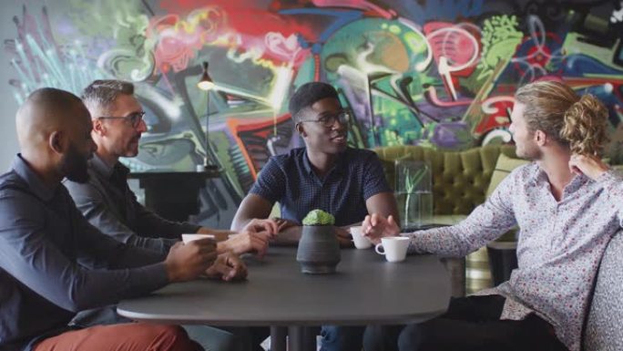四位男性创意同事在工作场所食堂的桌子旁聊天，特写