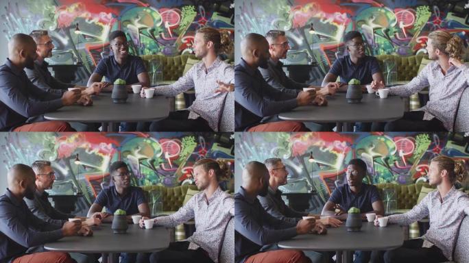 四位男性创意同事在工作场所食堂的桌子旁聊天，特写