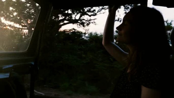 年轻快乐美丽的女游客微笑着，在日落森林的游览车里享受大气的野生动物园之旅。
