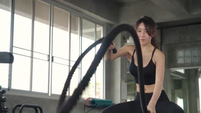 女人在健身房用战斗绳训练。强大的迷人的亚洲女性在健身房慢动作用绳索进行战斗锻炼。