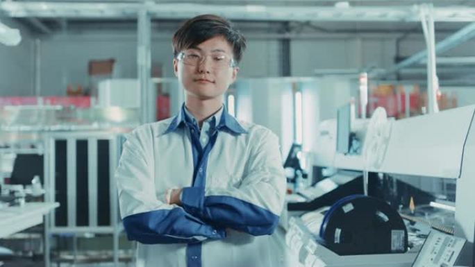 高科技工厂: 双臂交叉的亚洲工人肖像。在使用表面安装技术和拾取和放置机械的背景电子印刷电路板装配线中