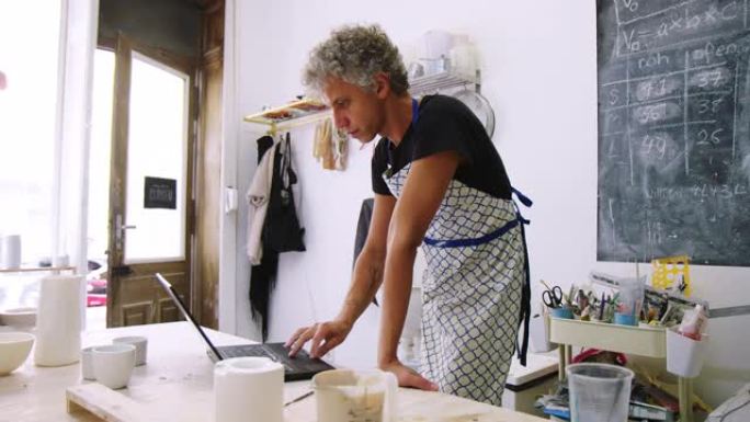 成熟的人陶器艺术家在艺术工作室使用笔记本电脑