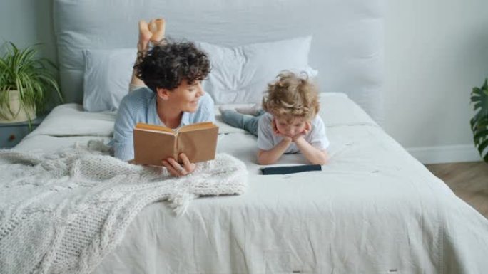 慈爱的妈妈看书，然后在卧室里用平板电脑和儿子一起看动画片