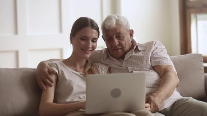 80年代快乐的男人拥抱成年女儿，看着电脑屏幕。