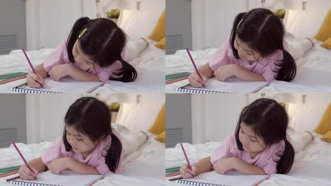 年轻的亚洲女孩在家画画。亚洲日本女儿童孩子放松休息乐趣快乐在素描本上画卡通睡觉前躺在床上，晚上在卧室