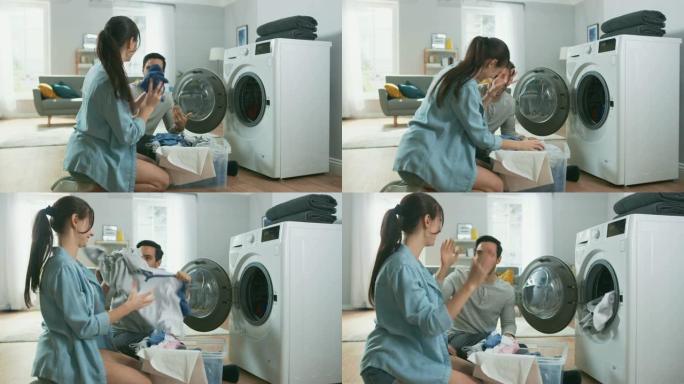 美丽的年轻夫妇坐在家里的洗衣机旁边。他们说话，给洗衣机装上脏衣服。明亮宽敞的客厅，室内现代。