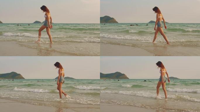 走在沙滩上的亚洲女人。穿着比基尼的年轻快乐女性在日落时放松和乐趣，在热带海边散步，度假，暑期旅行的概