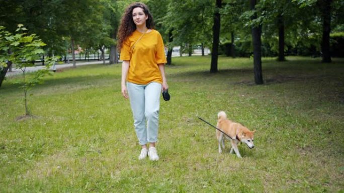 迷人的年轻女子和可爱的柴犬在草地上散步