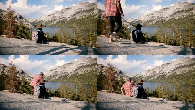 后视图旅游女孩坐在大石头的边缘，男人走上前，在优胜美地公园湖边坐在她旁边慢动作