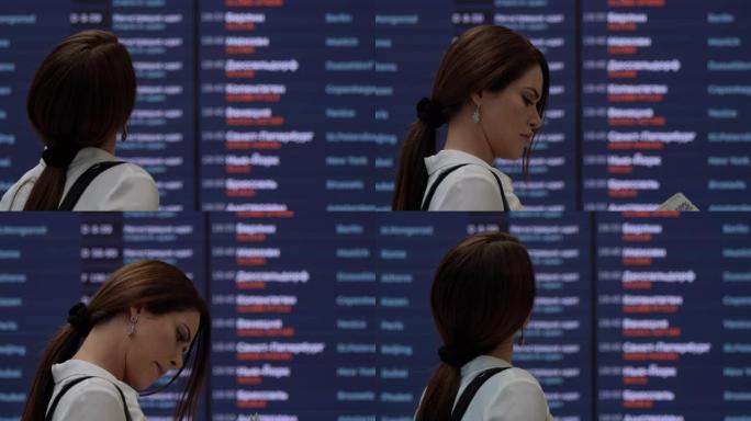 在机场看登机牌和航班时刻表屏幕的漂亮女人
