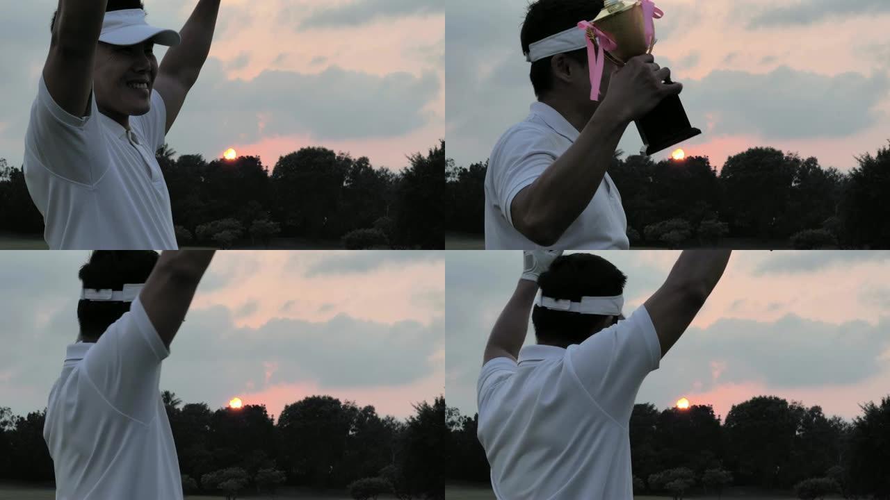 快乐的高尔夫球手拿着司机和奖杯，同时举起他的手臂与日落背景。成功的概念。体育电影