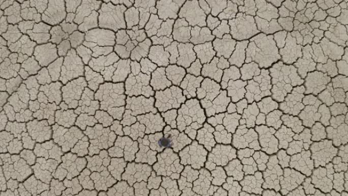 4k近景鸟瞰图，由于气候变化和全球变暖造成的干旱，一名饱受摧残的农民走过干燥大坝的图案化破裂的泥面