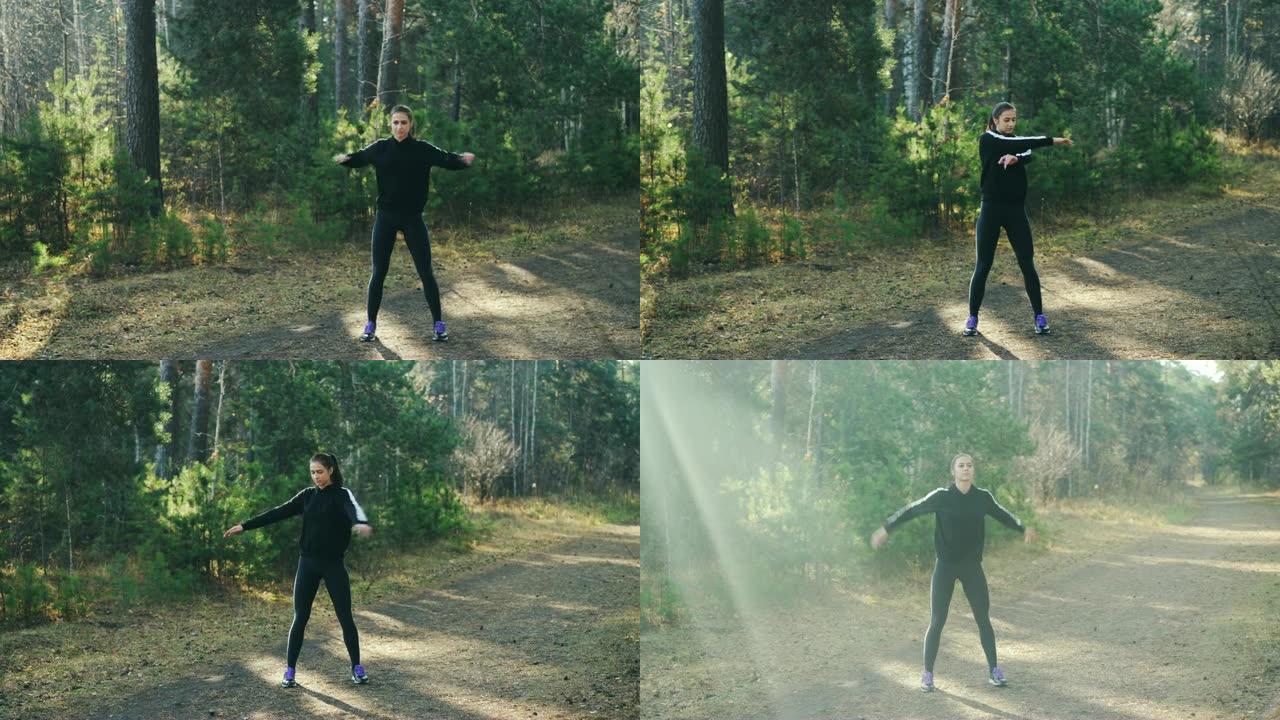 穿着现代运动服的漂亮年轻女子独自在公园热身运动，手臂和身体肌肉站在树木间的小径上。青年与体育观念。