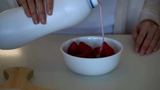 无法辨认的女人在一碗草莓上倒酸奶的特写