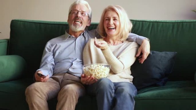 幸福的老夫妻拿着遥控器笑着看电视节目