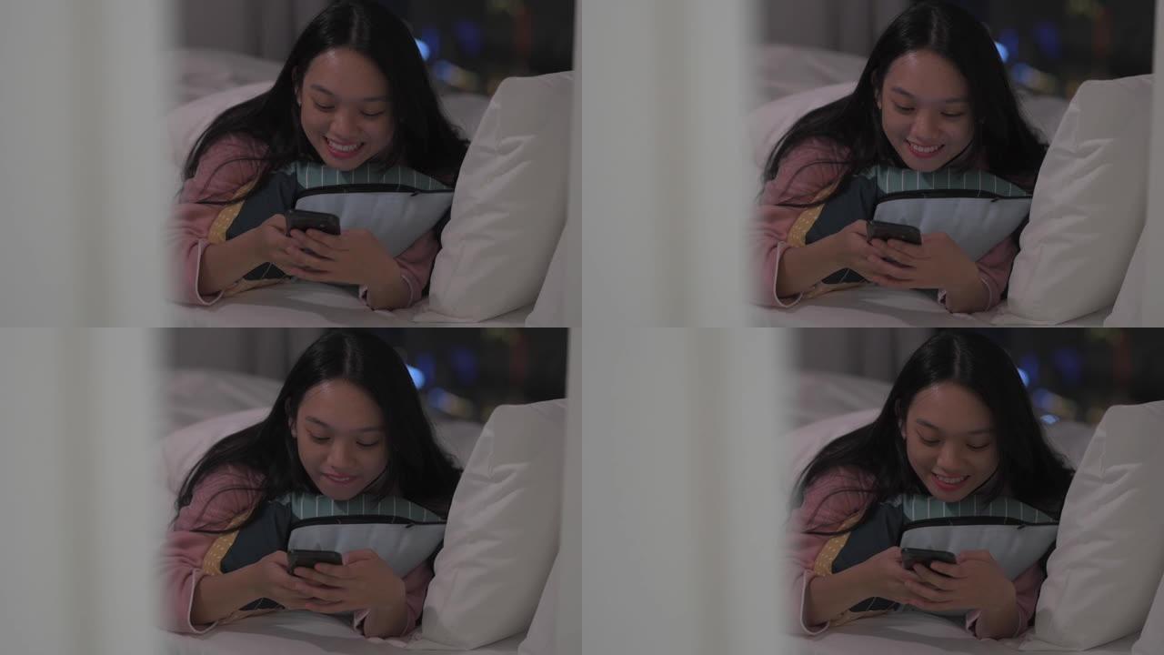 一名亚洲华裔女性在卧室的床上玩智能手机