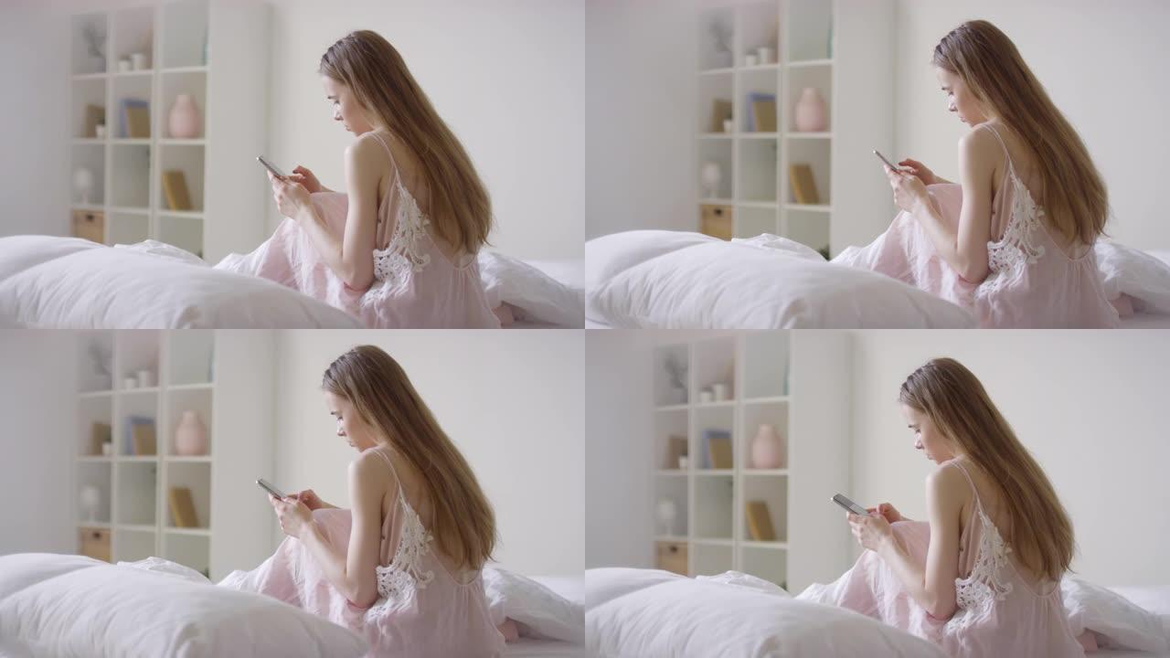 穿着睡衣的年轻女子坐在床上，用手机发短信