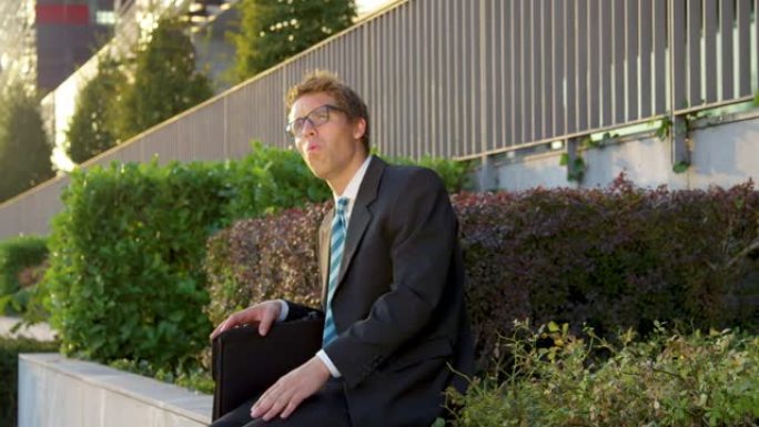 慢动作: 年轻的男经理坐在水泥壁架上吹口哨。