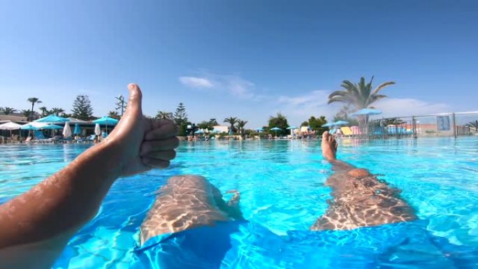 人坐在酒店附近的游泳池里竖起大拇指。暑假概念。