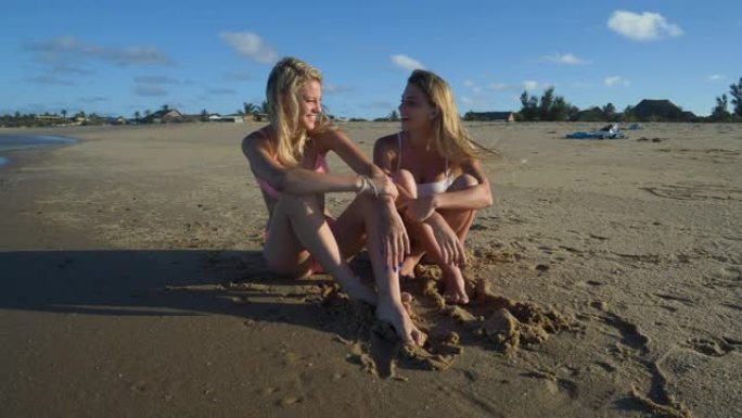 南非海滩上两个美丽的年轻女子笑着坐在海岸线上的4k前视图