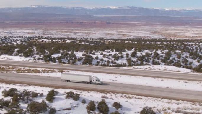 空中: 白色卡车将货物运送到风景秀丽的高速公路上，横穿雪白的沙漠