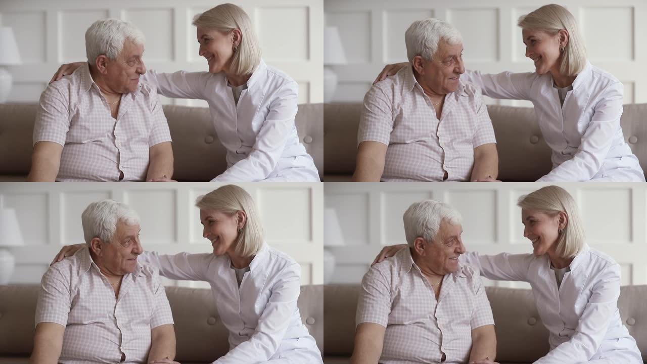 微笑的中年护士拥抱80年代男性患者的肩膀。