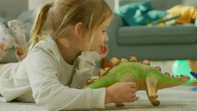 可爱的小女孩金发躺在家里的地毯上，玩玩具恐龙和飞机。快乐的孩子在阳光明媚的客厅里玩玩具。