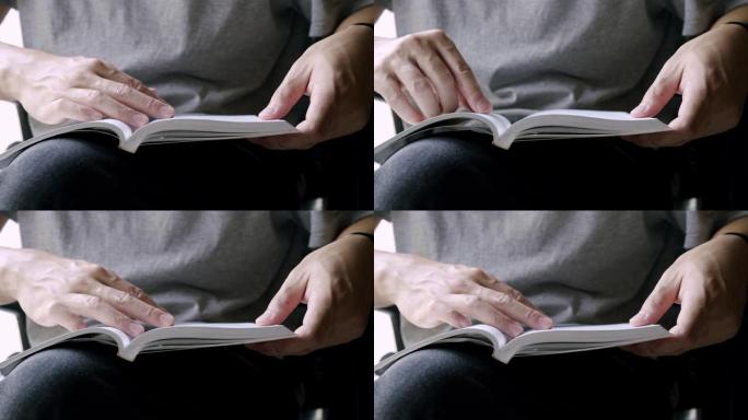 亚洲男人呆在家里一边读一本有趣的书。他翻页学习英语书。成年男子用手指指着一本书。