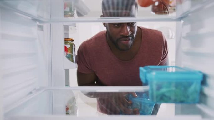 从冰箱里面看，当男人把健康的盒装午餐放在容器里时