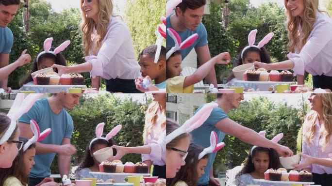 一群戴着兔子耳朵的孩子坐在户外的桌子上，与父母一起享受复活节派对-慢动作拍摄