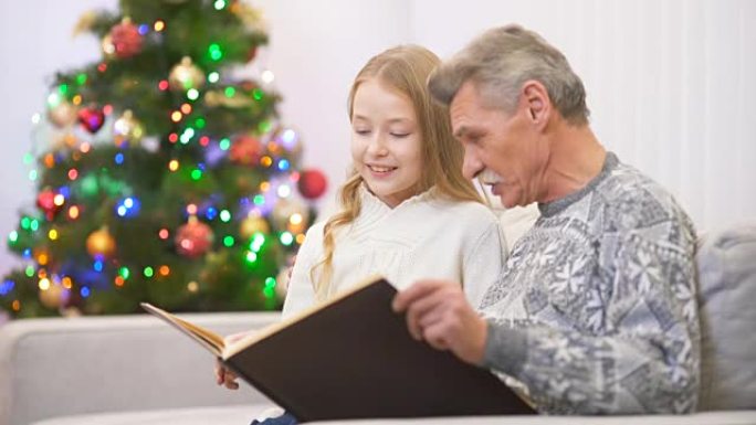 快乐老人在圣诞树旁与女孩一起看相册