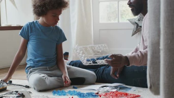 黑人中年父亲坐在家里的地板上，帮助他十几岁的儿子找到玩具建造套件的碎片，特写镜头