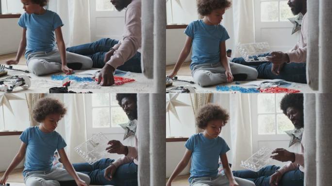 黑人中年父亲坐在家里的地板上，帮助他十几岁的儿子找到玩具建造套件的碎片，特写镜头