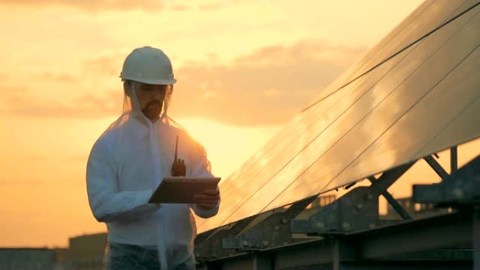 日落景观，男性建造师站在太阳能电池旁边操作计算机
