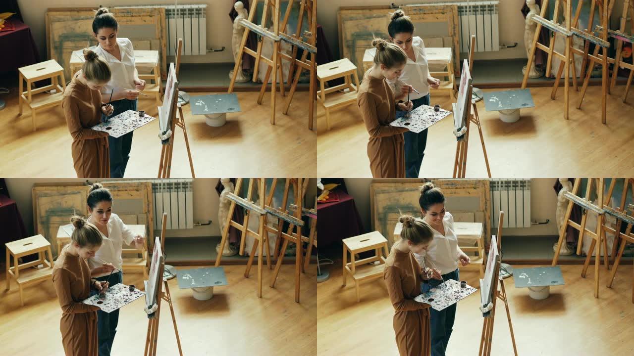 两位年轻女性艺术老师和学生在调色板上混合颜色，交谈和微笑，然后在modert艺术工作室的画布上绘画的