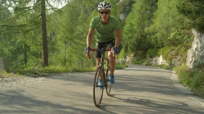 慢动作: 男性公路自行车手在阳光明媚的树林中踩踏陡峭的柏油路。