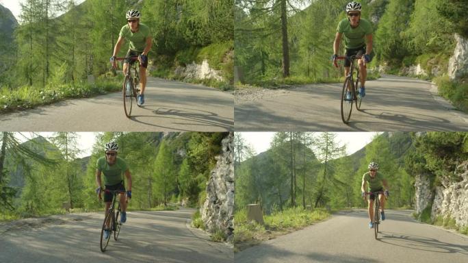 慢动作: 男性公路自行车手在阳光明媚的树林中踩踏陡峭的柏油路。