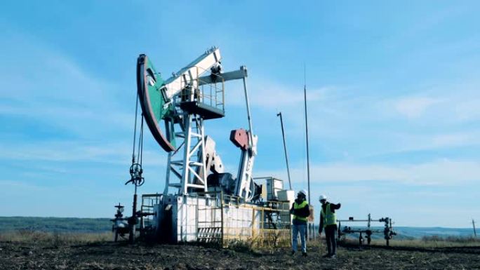 两个人检查一个正在工作的油塔。化石燃料，石油工业概念。