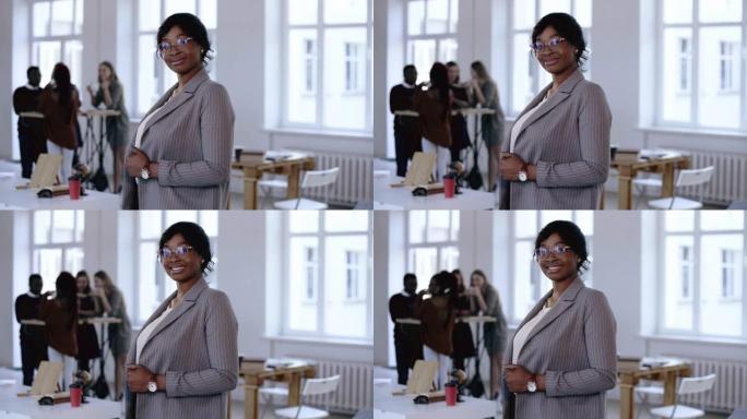 快乐的职业年轻黑人首席执行官商务女性穿着正式西装，眼镜摆姿势，在现代灯光办公室微笑。