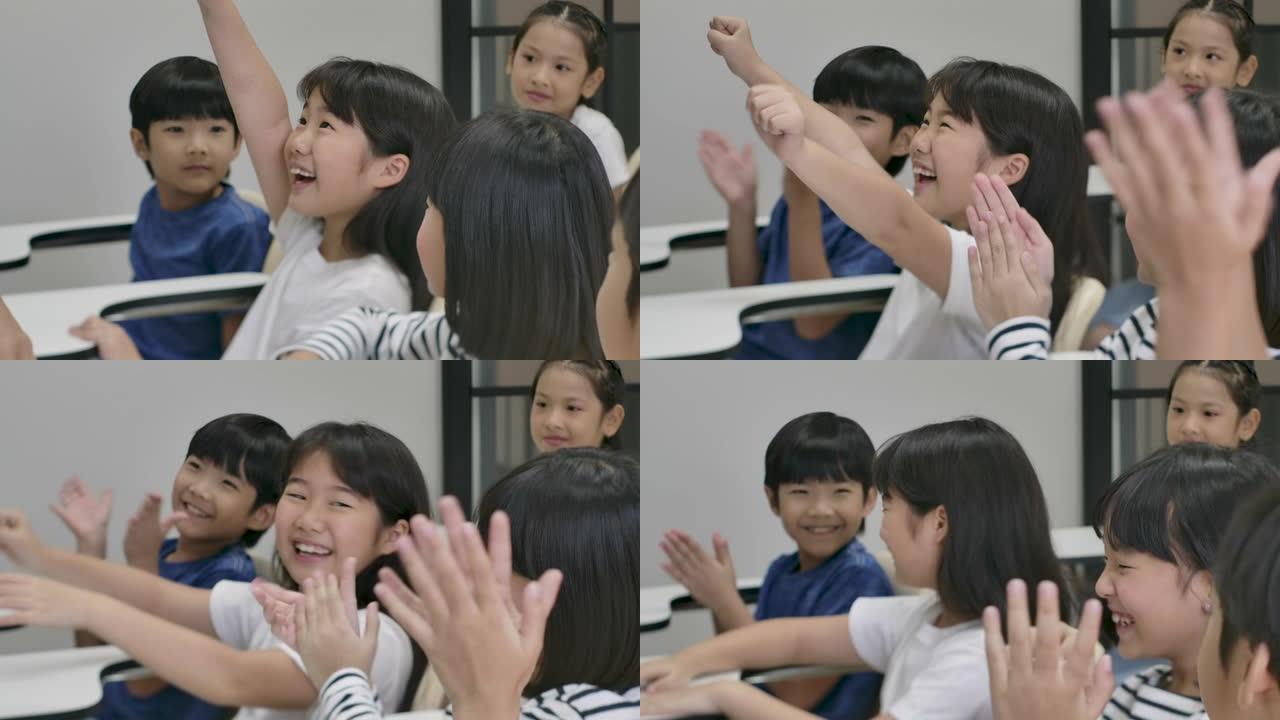 一群快乐的亚洲小学生举起手臂回答教室老师的问题。幼儿园学前概念。