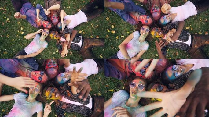 慢动作放大轻松的年轻人，脸上画着脸躺在草地上，伸手去拿相机移动的手，微笑着看着相机。乐趣和自然概念。