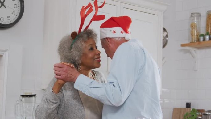 可爱的老年夫妇穿着化装礼服鹿角在厨房跳舞，同时准备圣诞晚餐