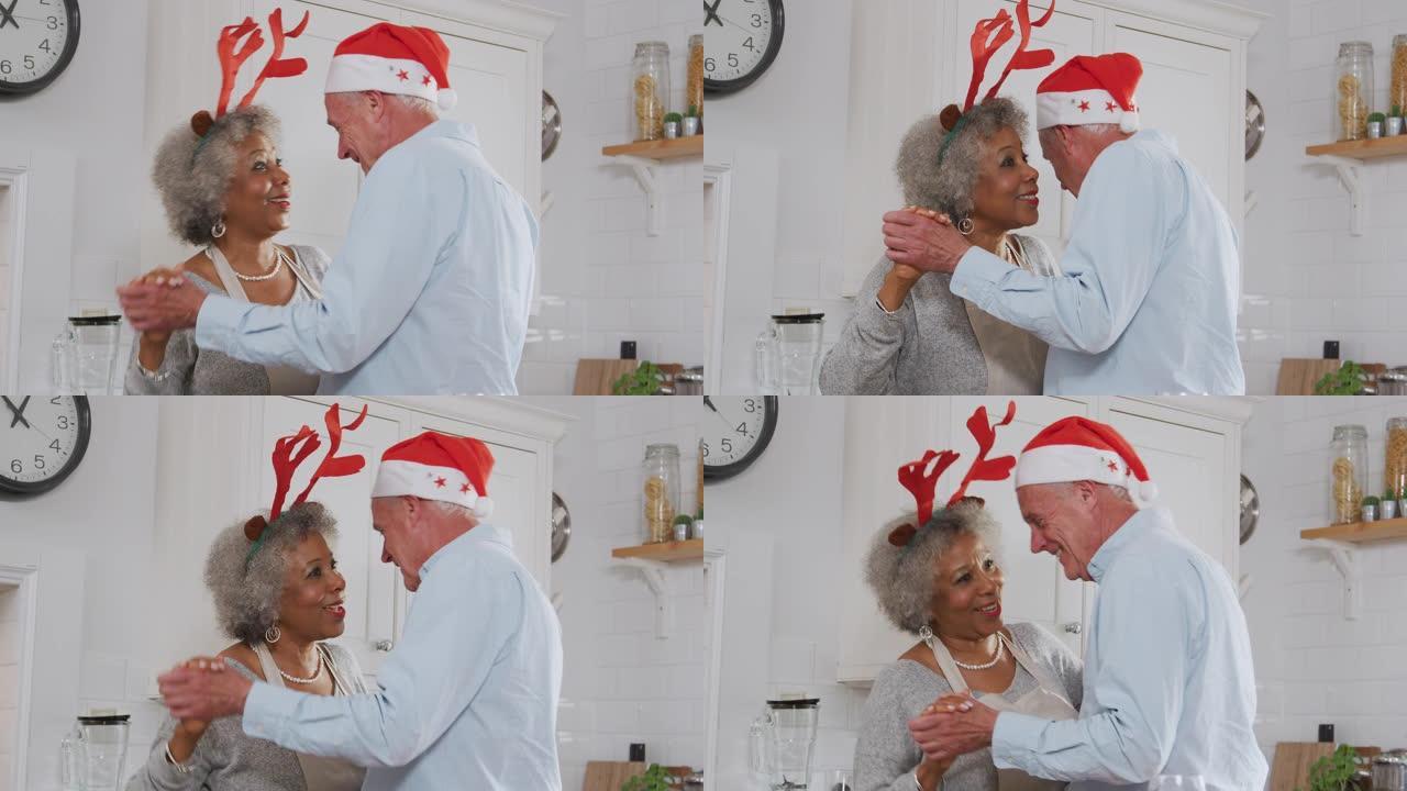 可爱的老年夫妇穿着化装礼服鹿角在厨房跳舞，同时准备圣诞晚餐