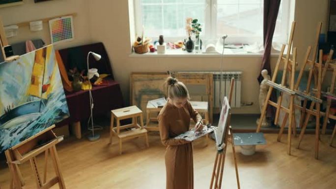 有创造力的人在艺术工作室用调色板和画笔上的油画绘画，女孩专注于工作。年轻女子穿着便装。