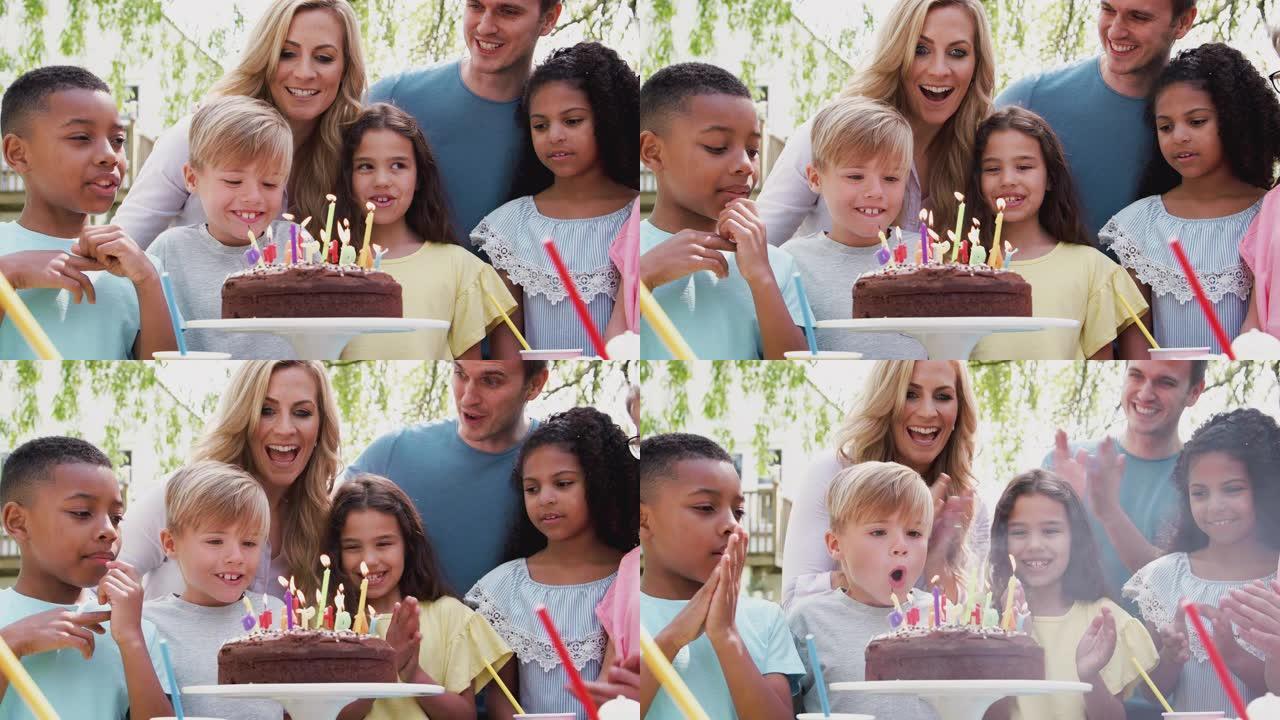 庆祝生日的男孩在花园里享受户外派对，父母和朋友在蛋糕上吹蜡烛 -- 慢动作拍摄
