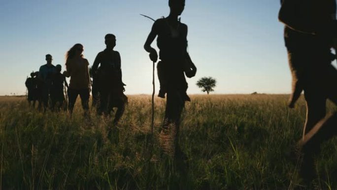 博茨瓦纳，一群游客在Makgadikgadi草原上与San人/Bushman穿着传统服装在丛林中漫步