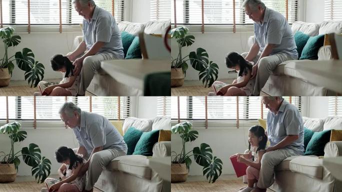 在家的泰国家庭: 祖父刷掉孙女的头发。迷人的小女孩微笑着，而祖父正在梳理孙女的头发。幸福的家庭。