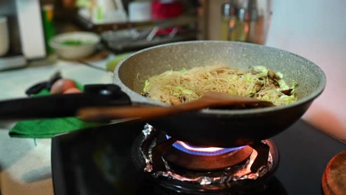 一个亚洲中国女性在家里烹饪中餐炒面在炉灶上烹饪平底锅