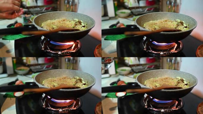 一个亚洲中国女性在家里烹饪中餐炒面在炉灶上烹饪平底锅